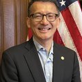 Commissioner Leung is a middle aged man standing in front of the US flag