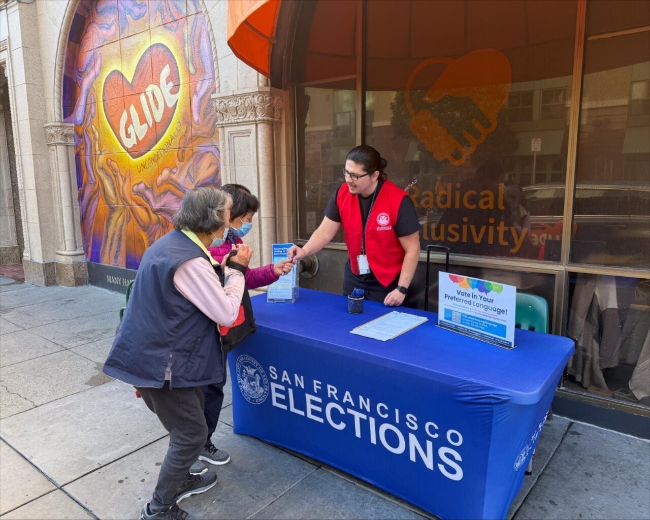 Department of Elections Outreach staff handing an SF resident a pen at a voter resource table.