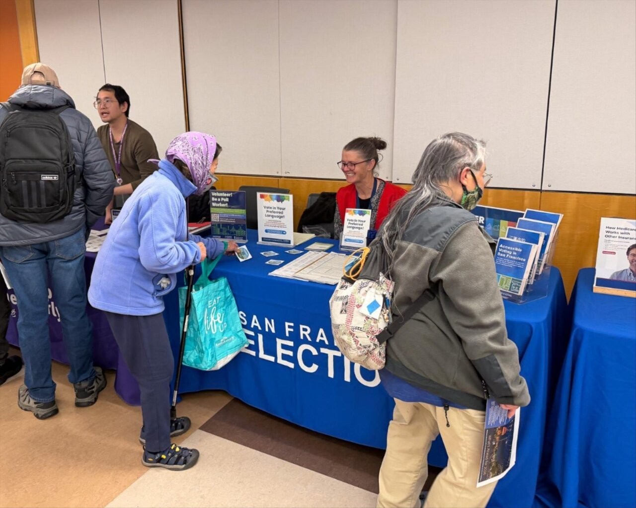 Outreach staff smiling at an SF resident as they grab a sticker from voter resource table.