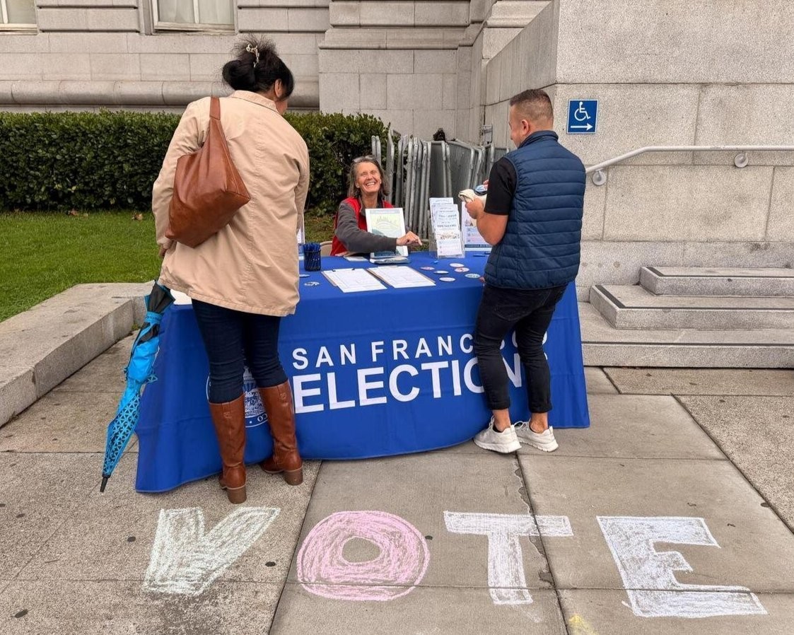 Department of Elections Outrach Staff tabling at an event and speaking with two members of the public about voting options.