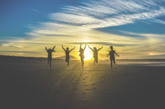 A photo of the silhouette of a group of people jumping on a beach, backlit by the sunset