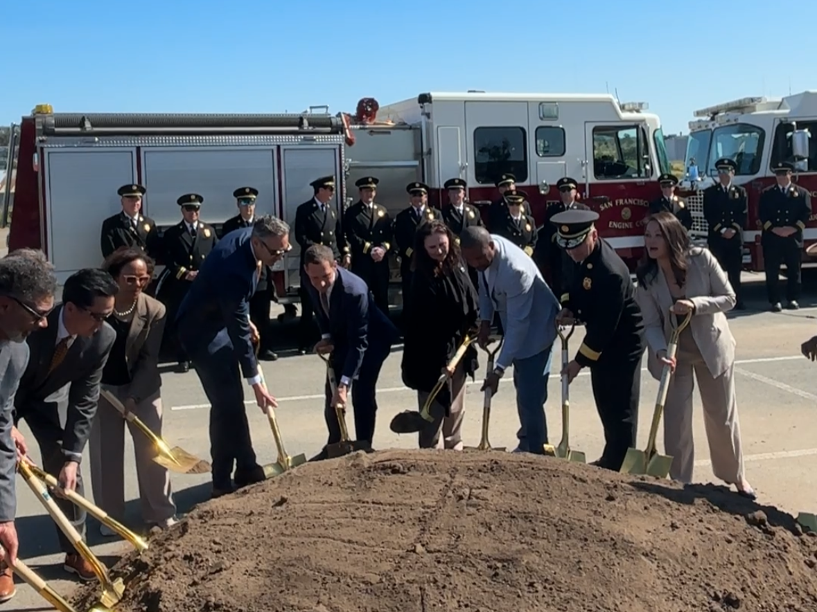 A group shovels dirt in front of a firetruck.