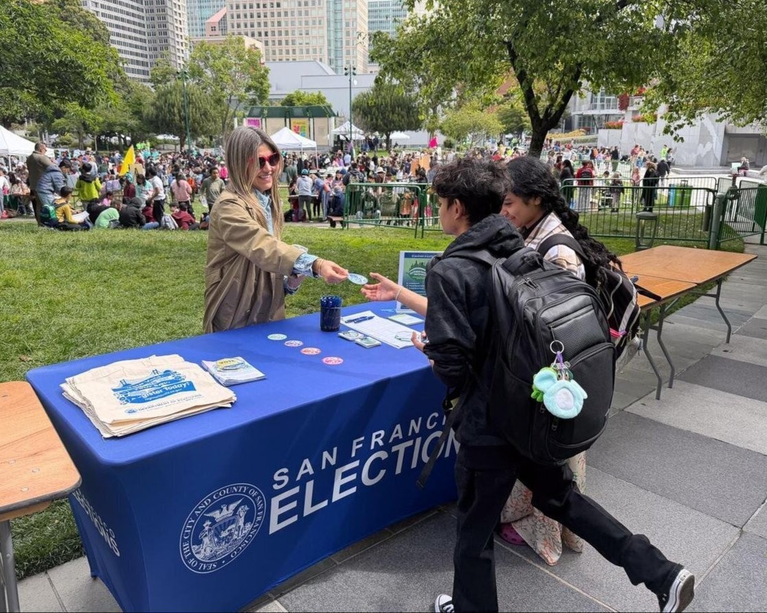 Department of Elections Staff handing a sticker to students.
