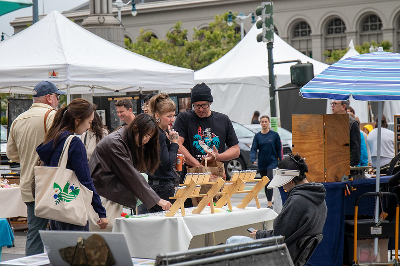 People shopping and looking at artist's goods for sale outdoors with white tents