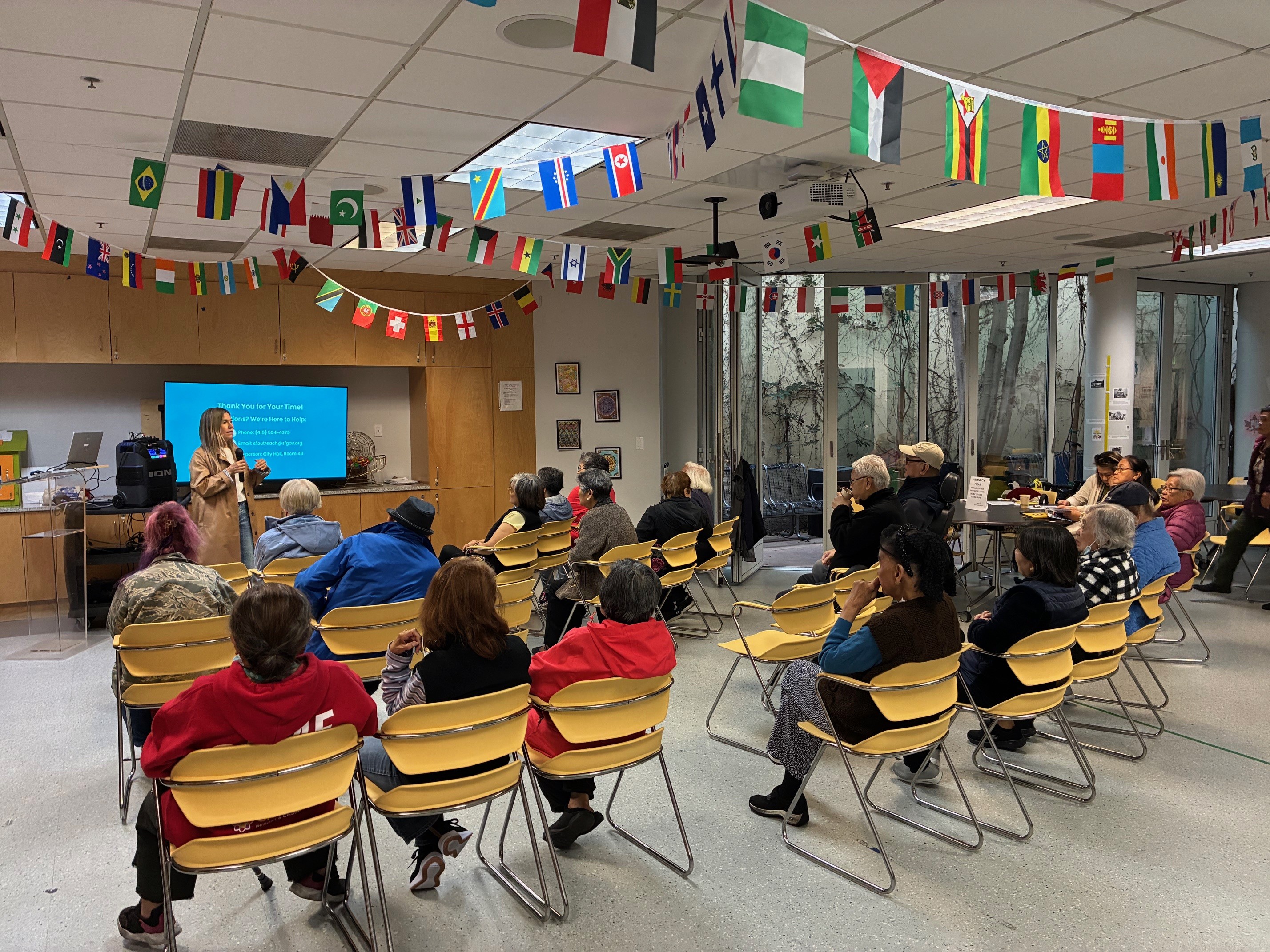 2 rows of senior citizens sitting and watching an election presentation given by and outreach coordinator.
