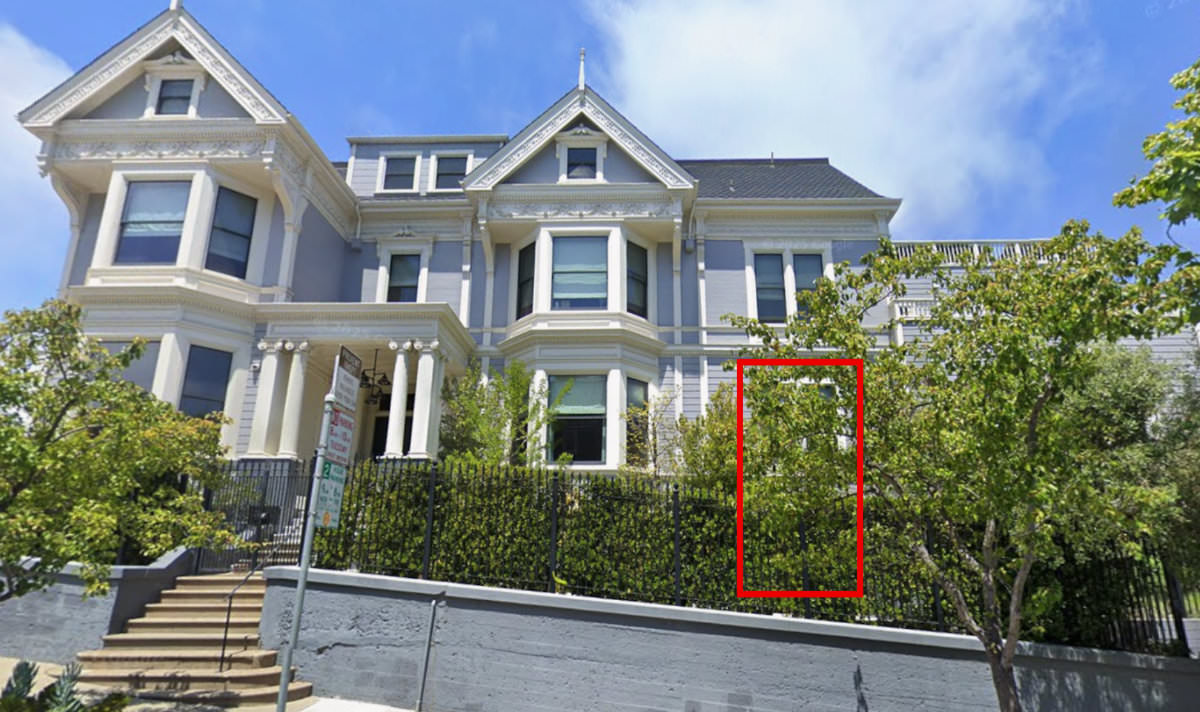 A house with a red box drawn over window, where the window cannot be directly seen because a bush and tree are blocking it.