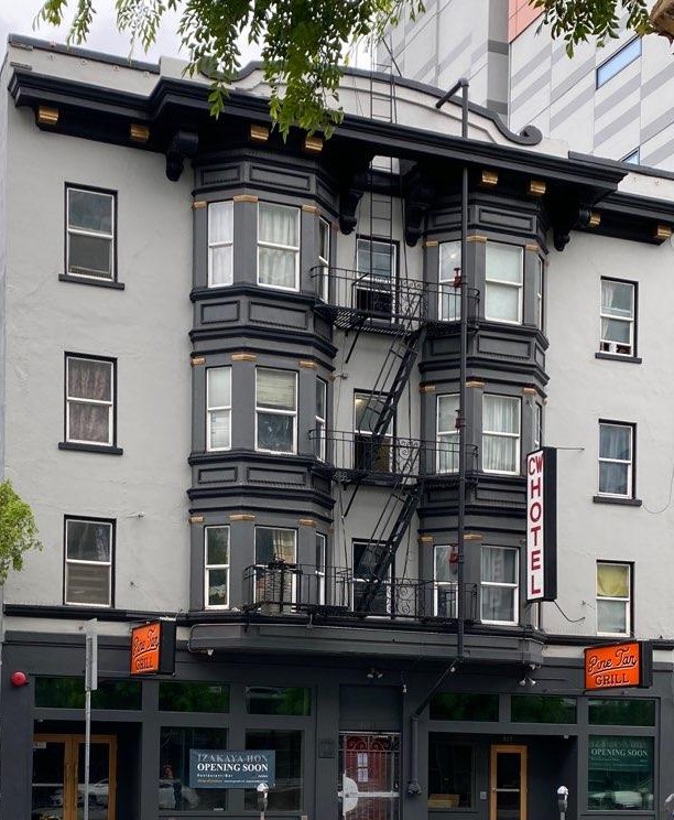 grey and dark grey building that has a white sign with red lettering reading - the CW Hotel is located here CW Hotel