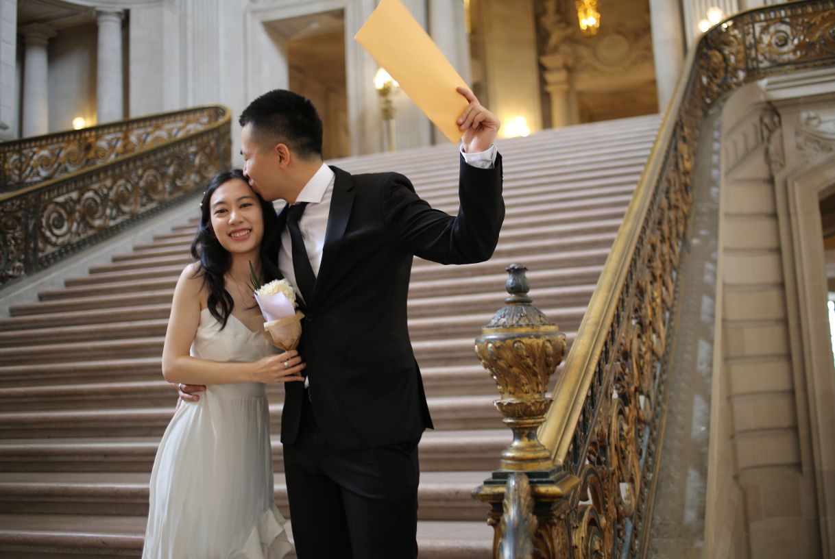 Couple on steps of SF City Hall holding marriage license.