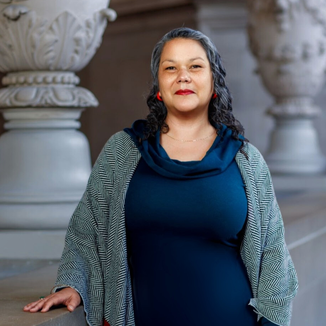 Woman with black and grey shoulder length hair wearing a navy dress and shawl