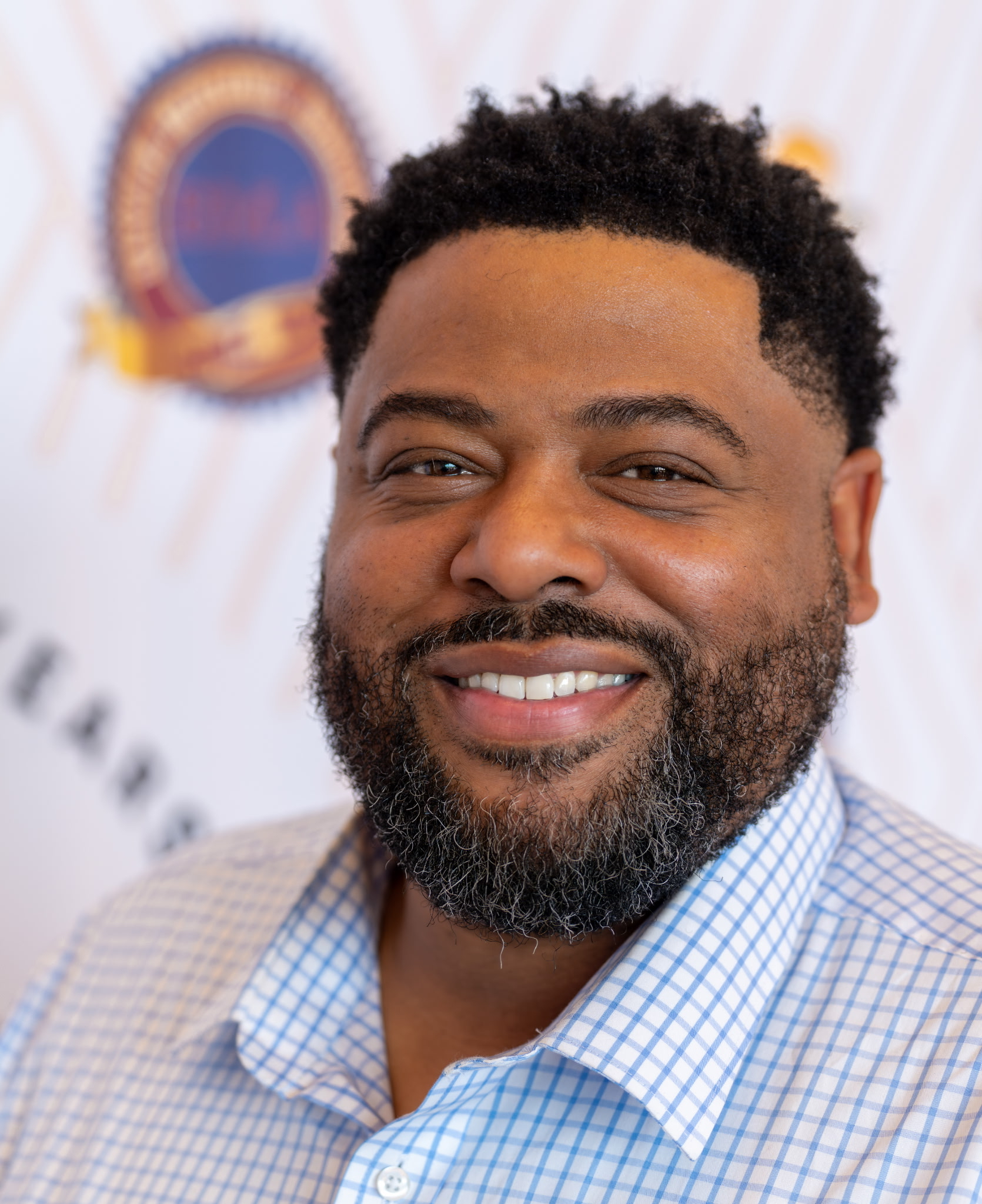 A headshot of Commissioner Dontaye Ball in a blue and white checkered button up shirt.