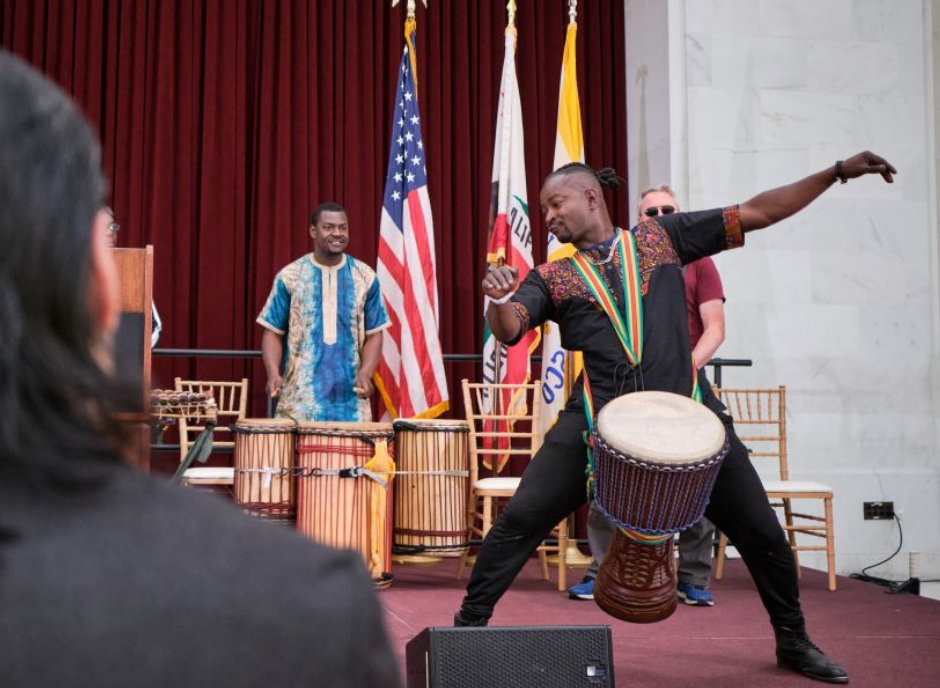 Man plays African drum with backup drummers on stage