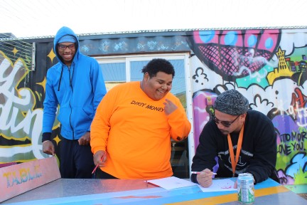 3 youth talking and smiling in front of a mural.