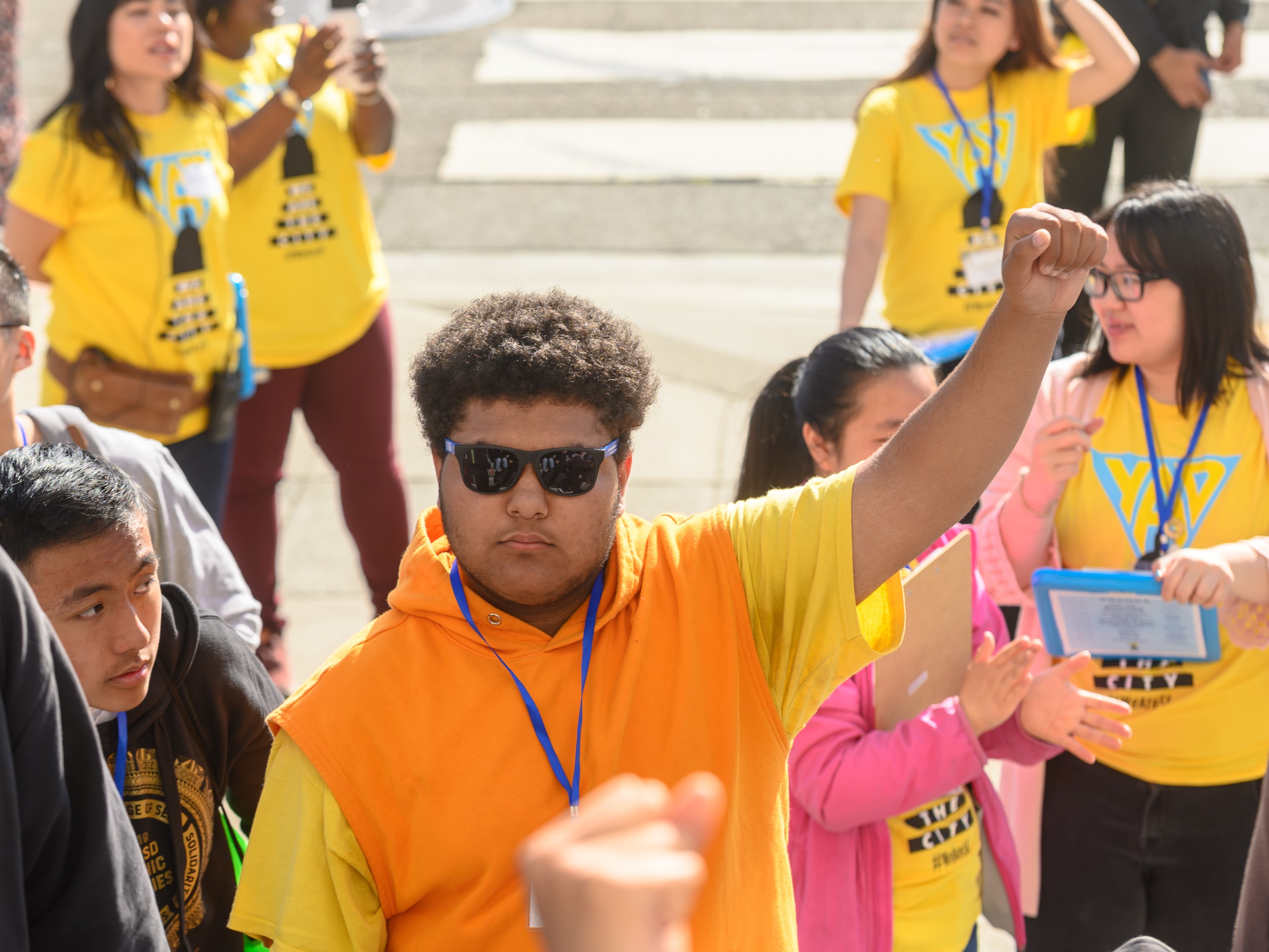 A teen standing on the steps of a building with 1 fist raised to the sky