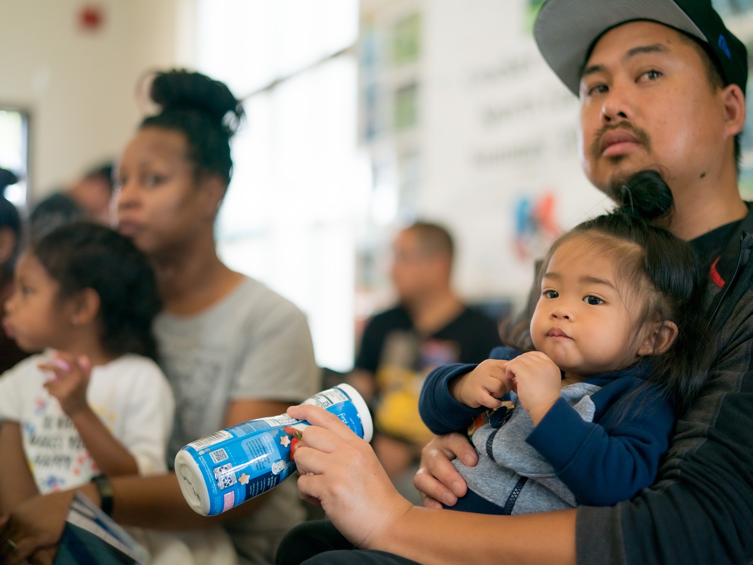 A man with a baby on this lap with a mom in the background with her child