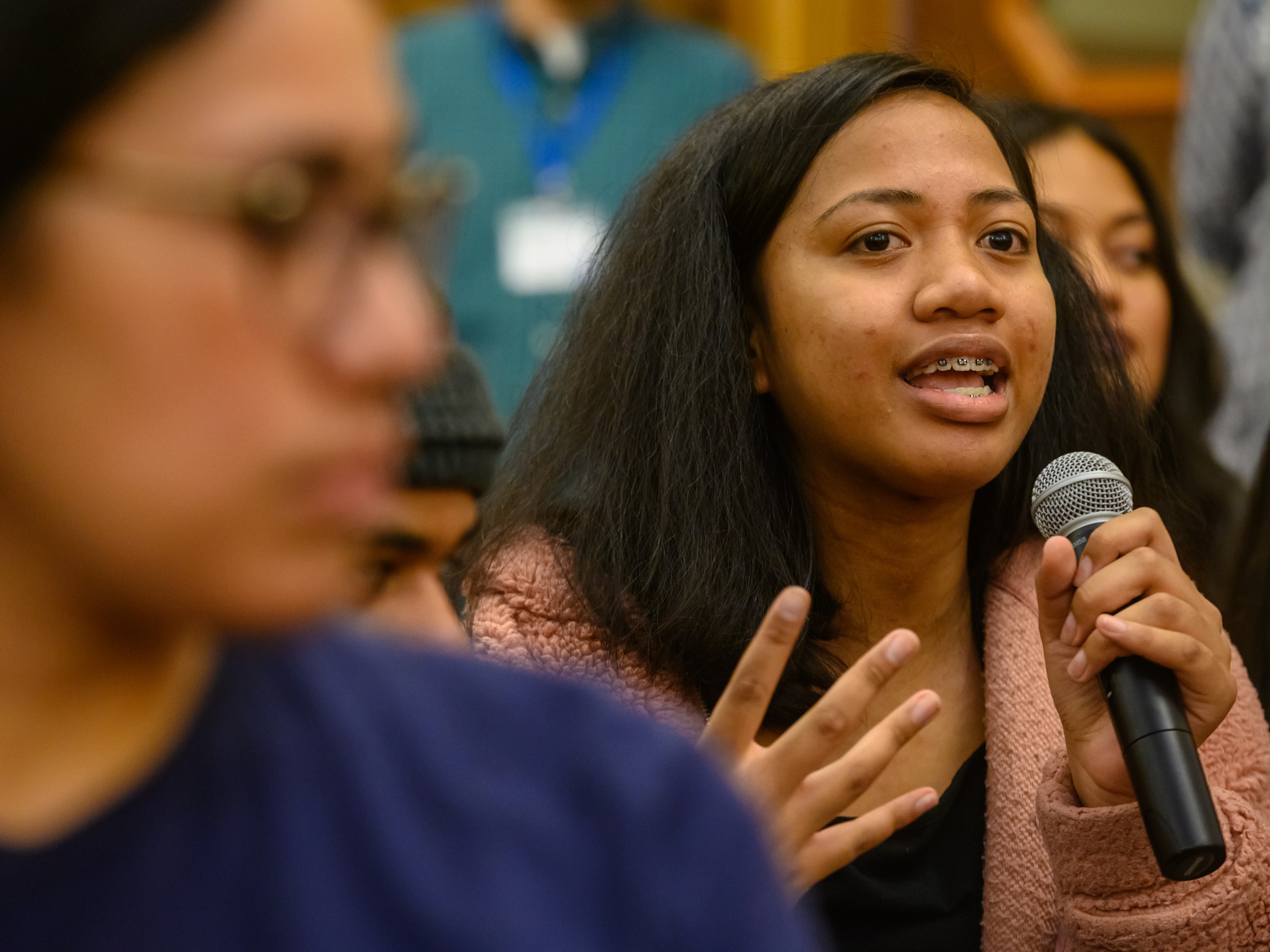 isang tinedyer na babae na nagsasalita sa mikropono habang nakikinig ang ibang kabataan