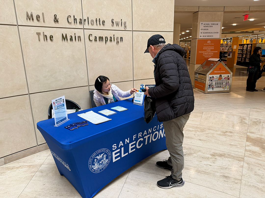 Picture of Elections Outreach staff speaking with an SF resident at the SF Public Library Main Branch lobby.