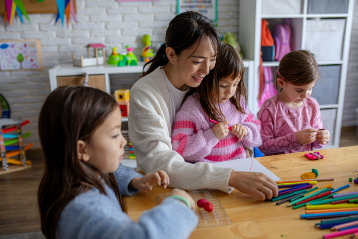 Young children develop fine motor skills and creativity while working with clay and crayons under teacher supervision in a preschool environment