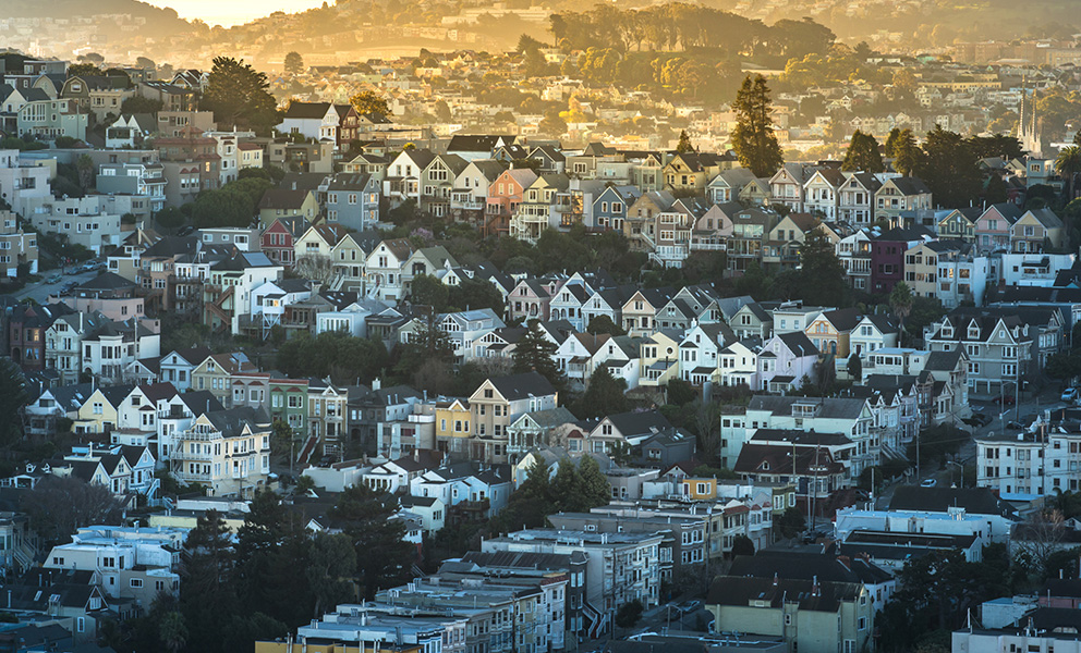 A dense hillside neighborhood of colorful homes in San Francisco is bathed in warm, golden light.