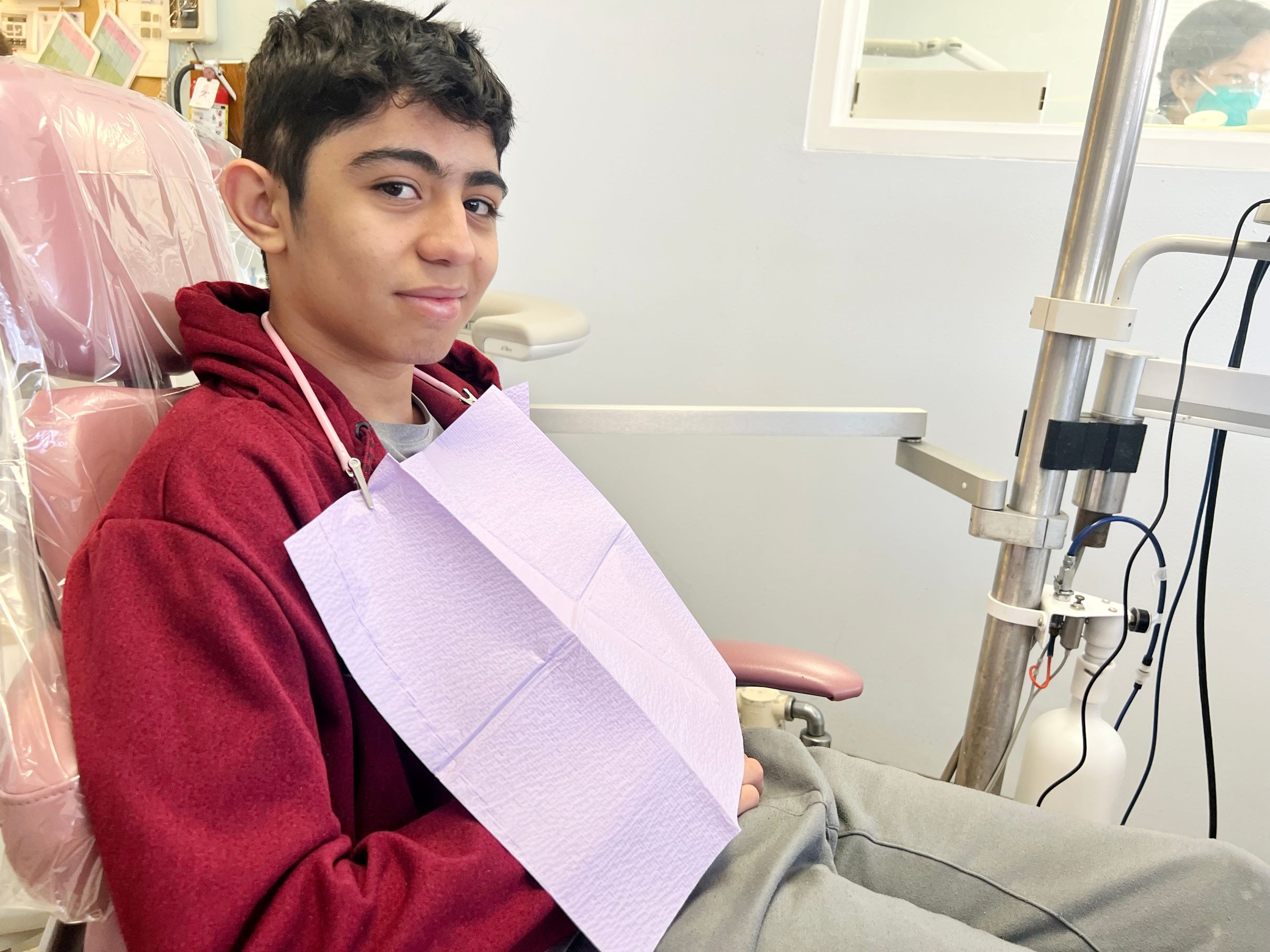 A boy in a red sweater with a disposable dental bib sitting in a dental chair