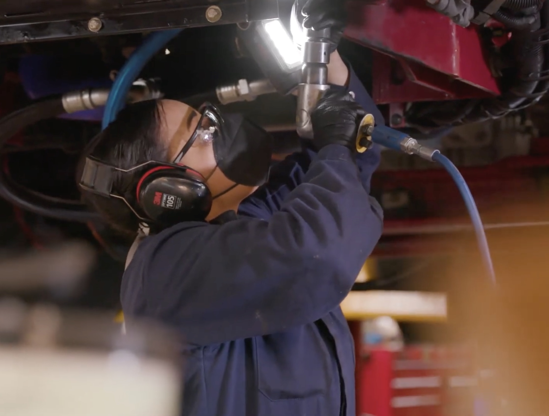 Jamice Jones in a navy uniform working on the underside of a red fire truck.