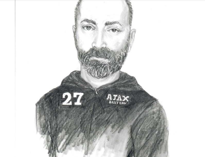 A black-and-white pencil sketch of a man with a beard and short hair. He is wearing a hoodie with the text 'AJAX EAST BAY' on the left side of the chest and the number '27' on the right. The expression on his face is neutral, and the drawing is detailed, with shading emphasizing depth and texture.