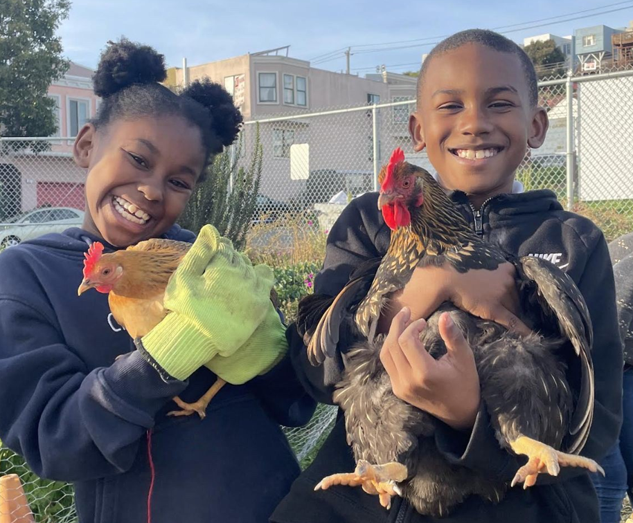 two smiling kids hold chickens at the Florence Fang Community Farm in the Bayview