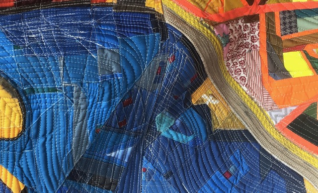 Close-up of a textured textile artwork with layered fabrics, stitching, and abstract shapes forming a detailed, patterned surface.