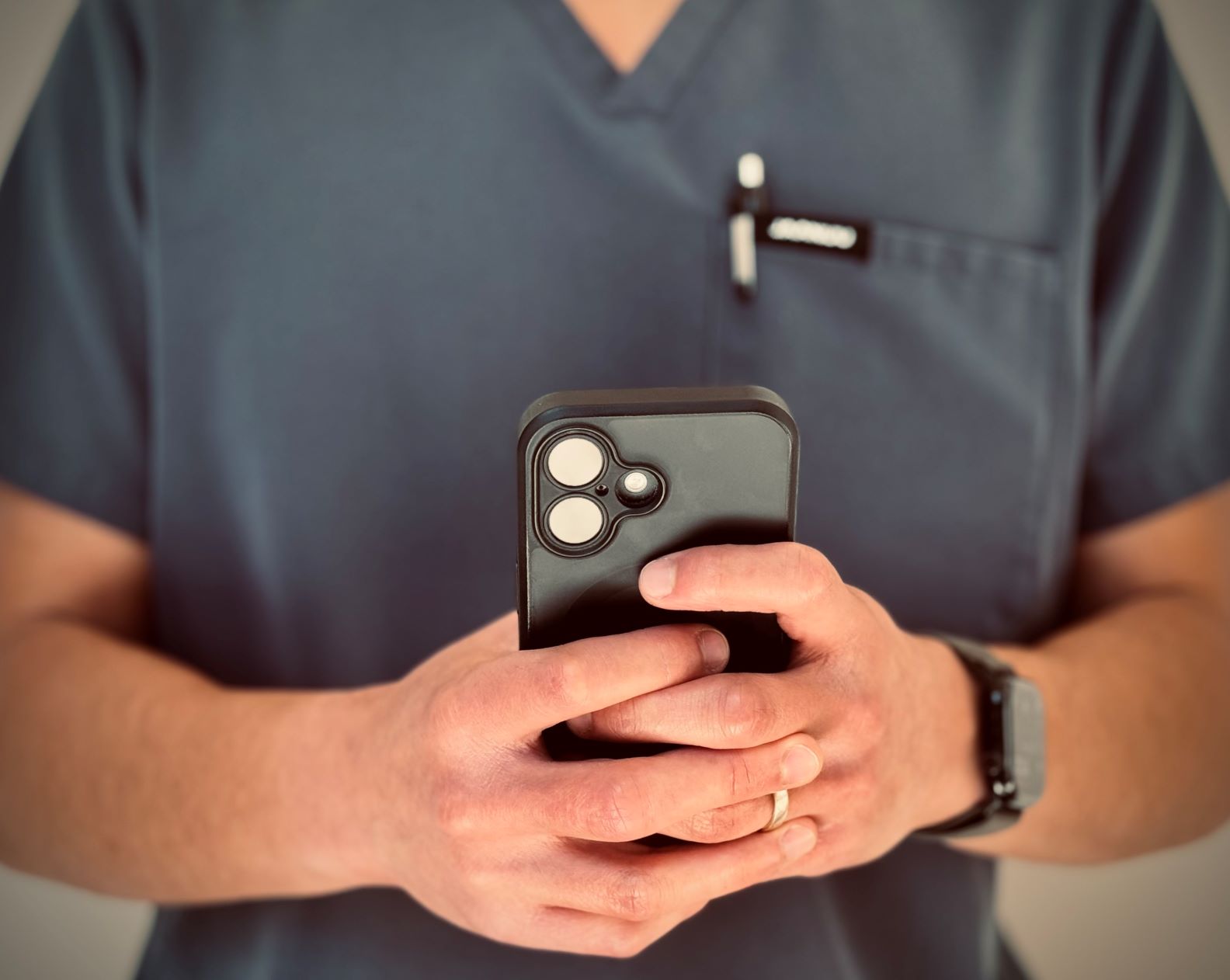 Zoomed in view of someone in dark grey scrubs holding a cell phone