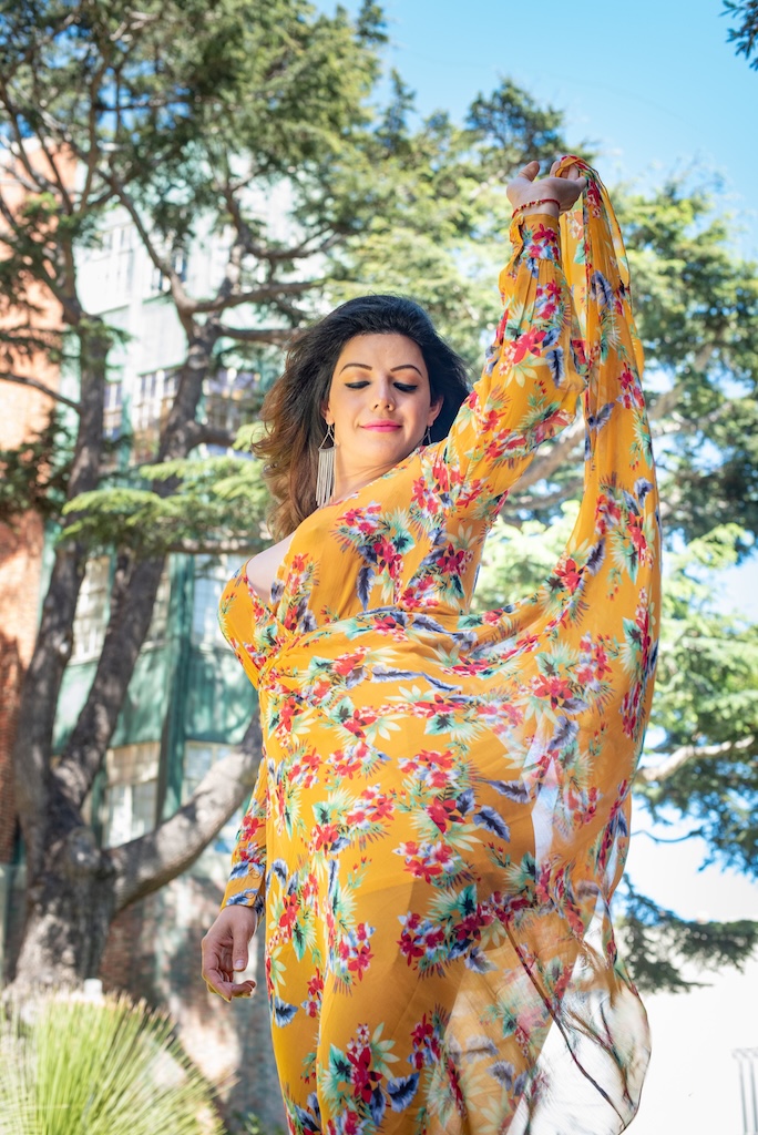 Latina trans woman wearing a flowy yellow dress posing gracefully