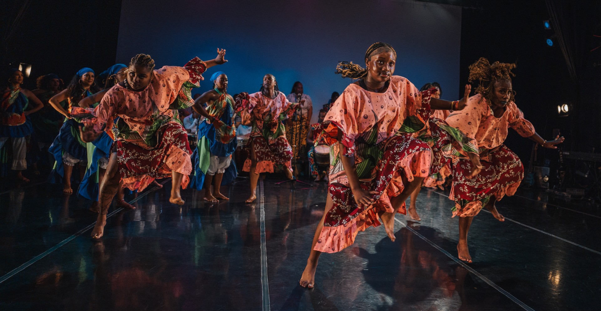A group of dancers dressed in orange attire leap in midair.