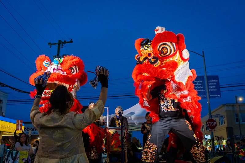 Two lion dancers perform in front of a stage.