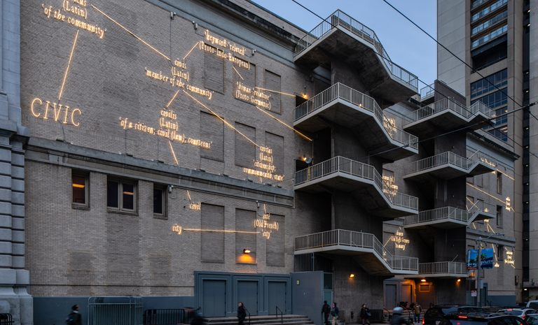 Urban building façade with exterior staircases, illuminated text and diagram-like projections spread across the brick wall.