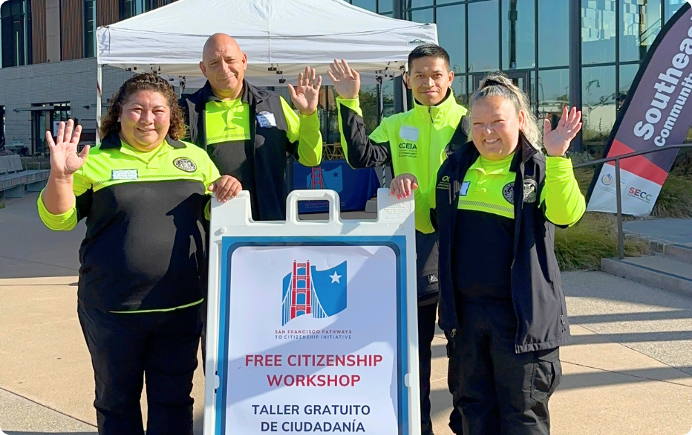 Four Community Ambassadors wearing high visibility yellow uniforms smile and wave as they welcome participants to an SF Pathways free citizenship workshop.