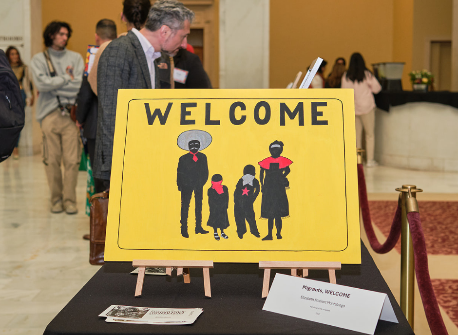 Artwork on a stand on a table, artwork reads WELCOME over yellow background with silhouettes of a mariachi group