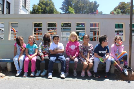 Kids sitting on a bench in a school yard.