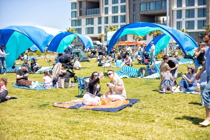 People picnicking at Cityside Park under blue tents on a sunny day
