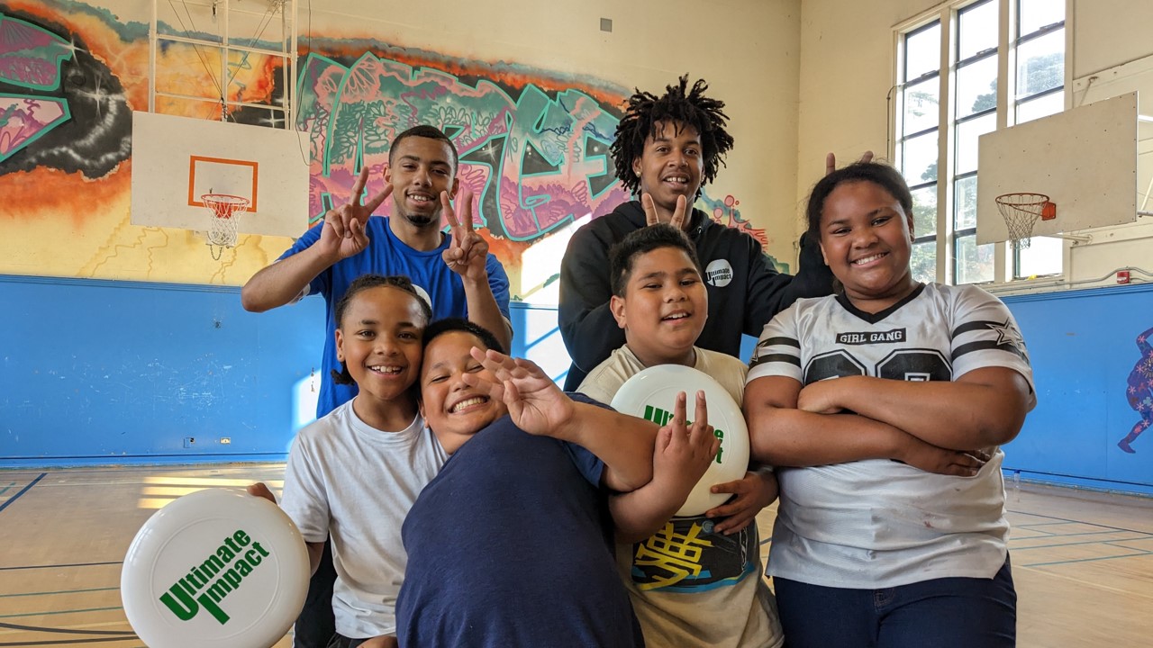 a group of smiling youth participants pose holding frisbees inside a gym