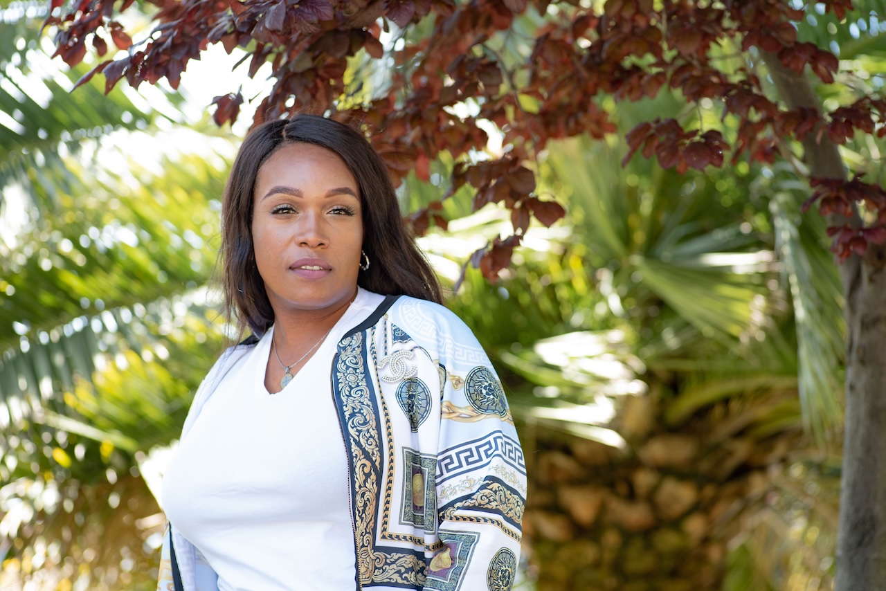 African American trans woman wearing a white blouse posed in front of some foliage