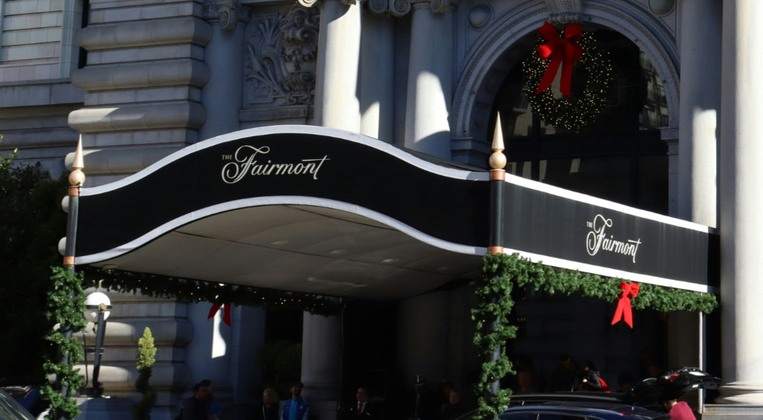 A curved fabric canopy over the front entrance of a hotel, with its support columns covered by holiday garlands.