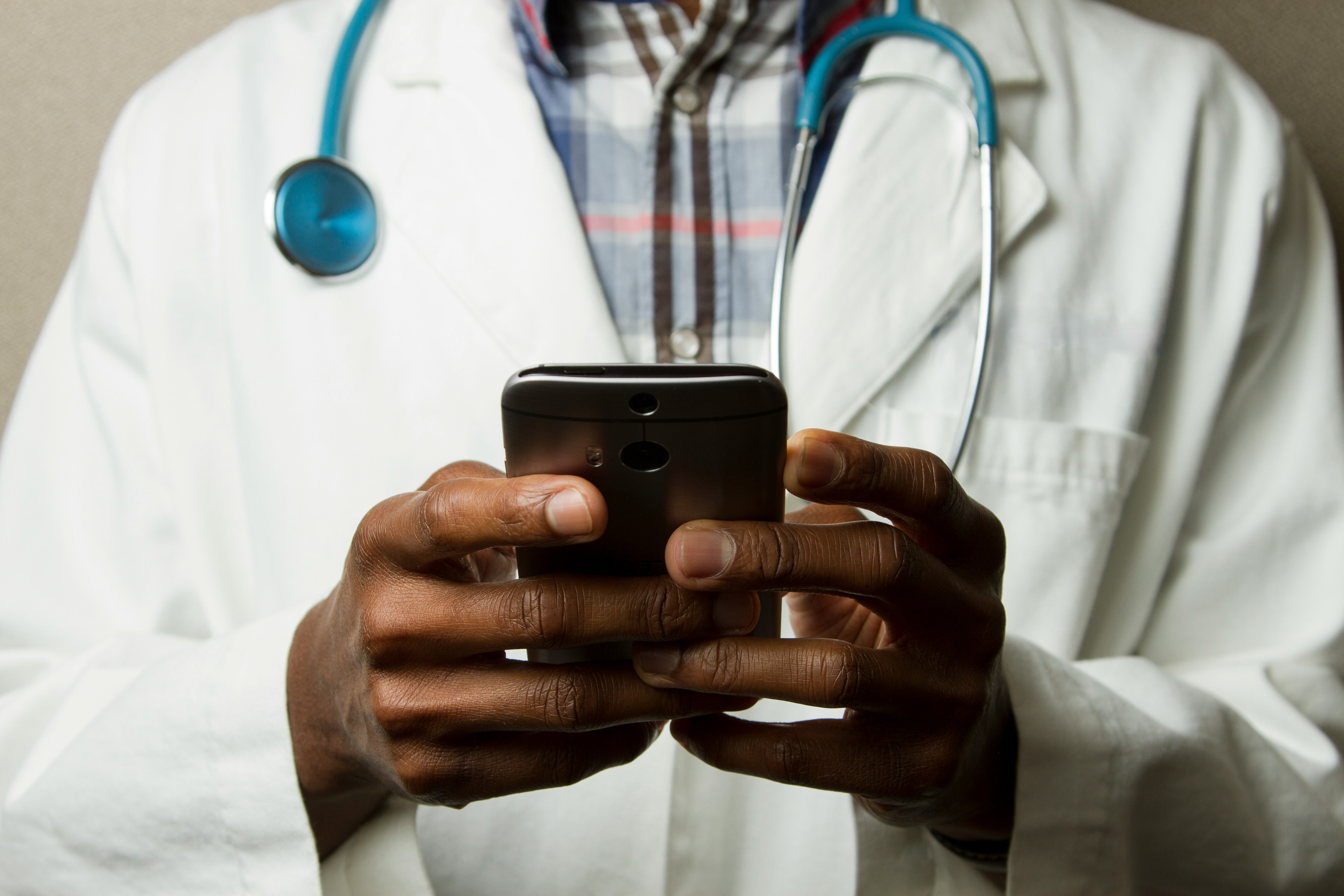 zoomed in view of someone in a white coat with a stethoscope around their neck holding a cell phone