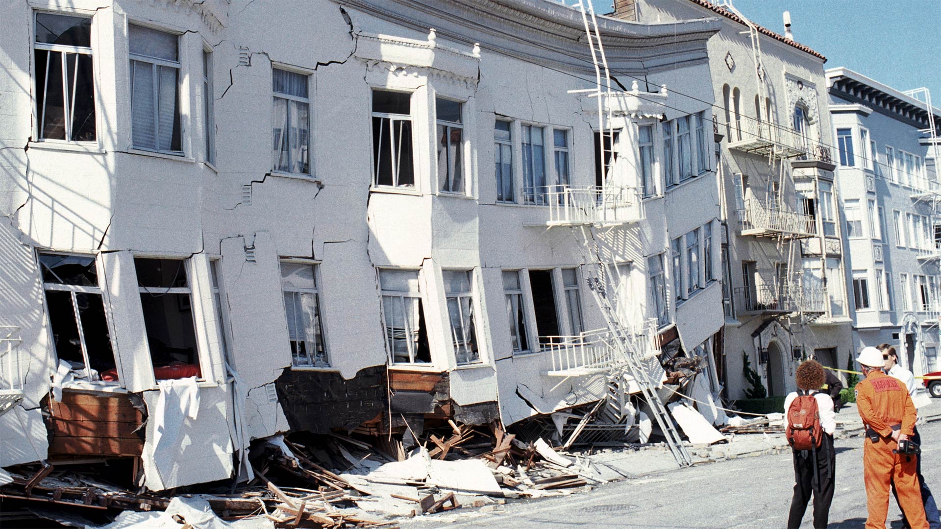three people stand in front of a destroyed building
