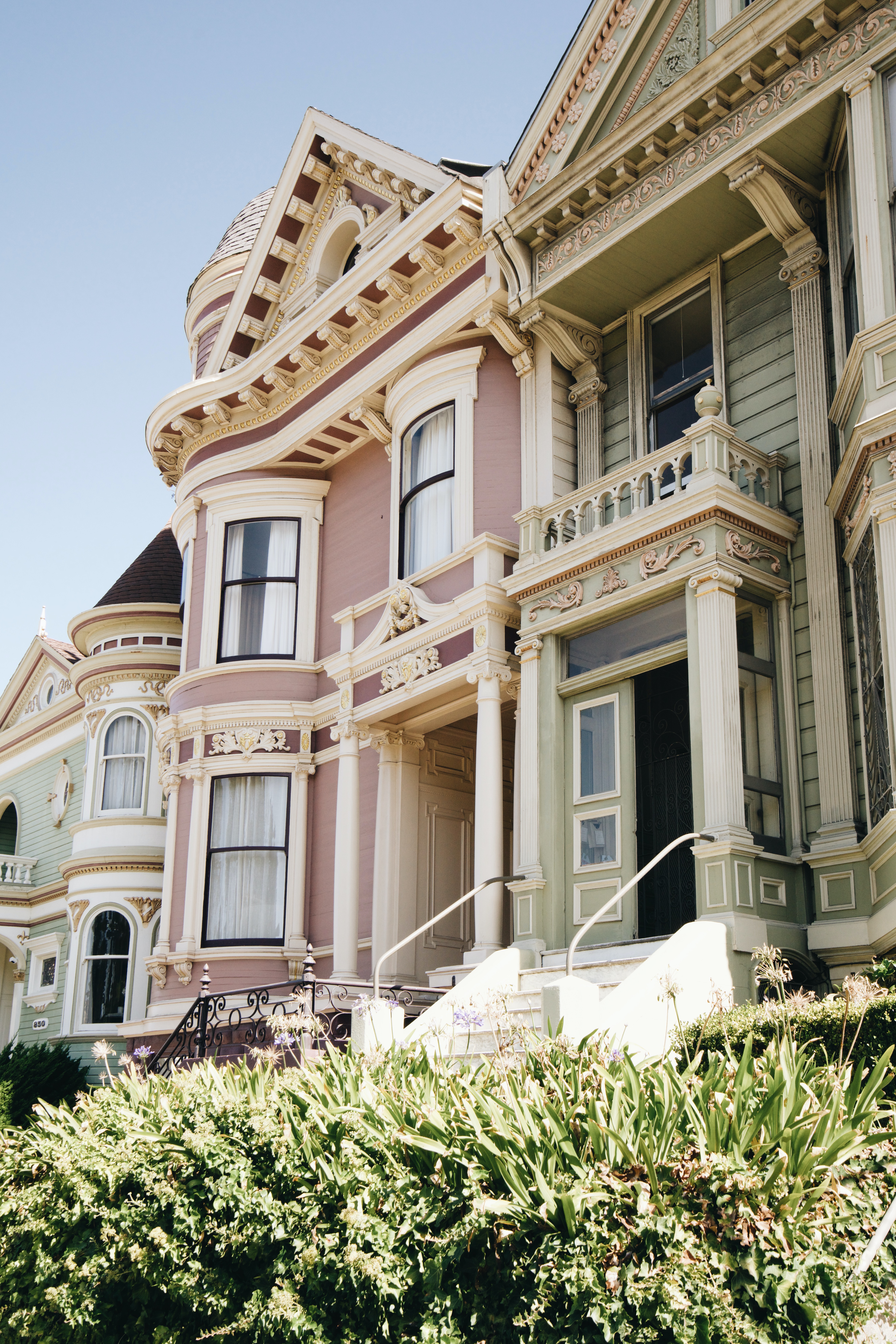 Several victorian style homes in a row, with bushes in the front