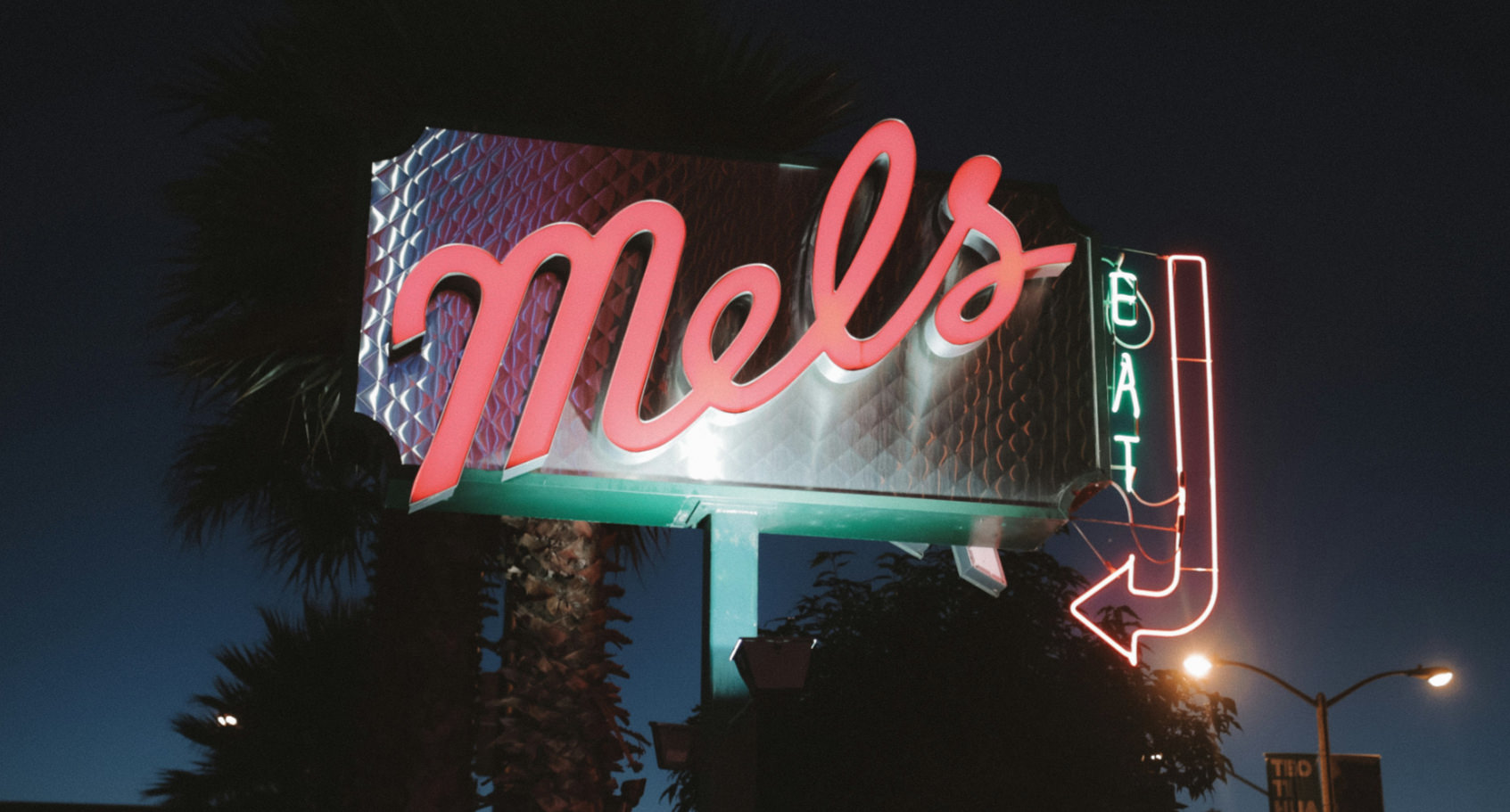 A large freestanding ground sign shown at night, with a combination of colorful neon lighting, a translucent cabinet, and a large spotlight shining on it from below.