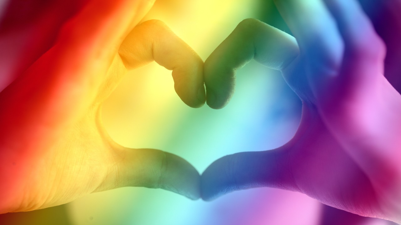 Two hands making a heart in rainbow light