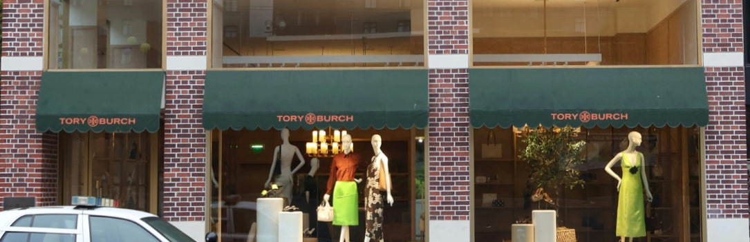 Multiple dark green fabric awnings above the windows of a retail store, supported only by the metal structures against the building.