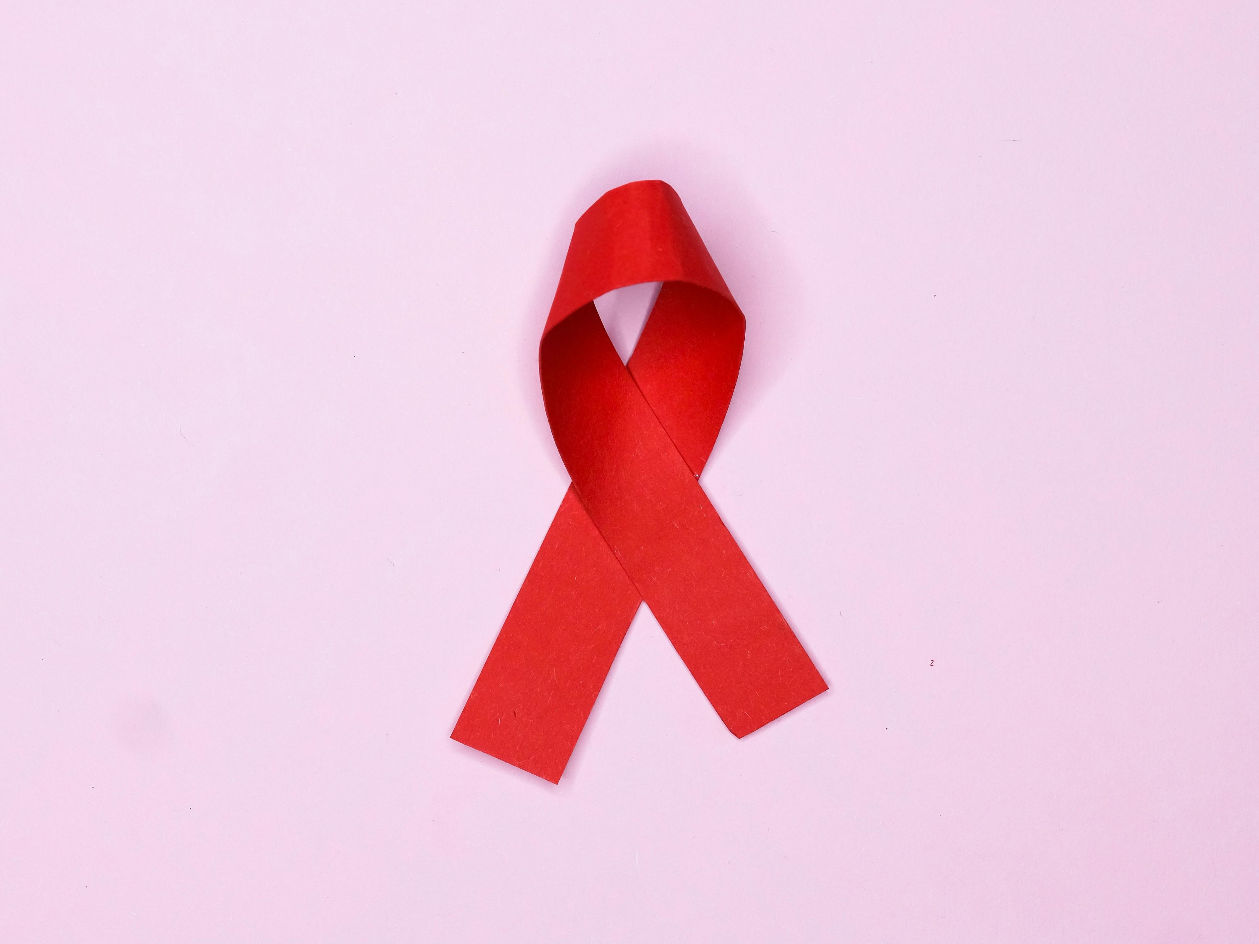 a red HIV awareness ribbon on a pink background