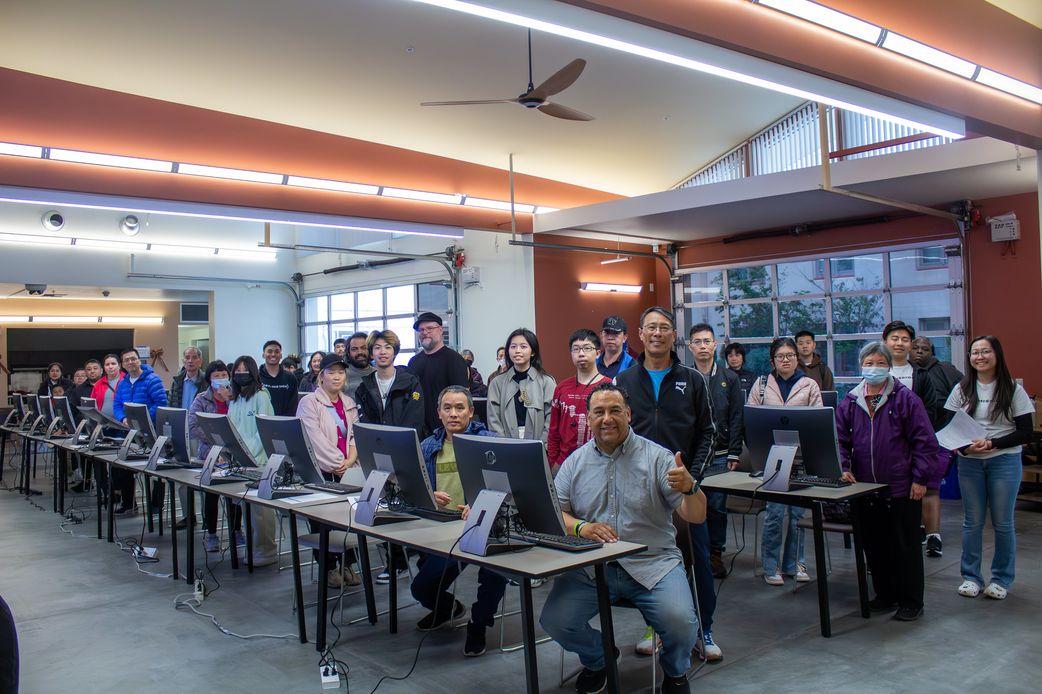 Group of class participants and organizers with desktop computers in a community workshop space.