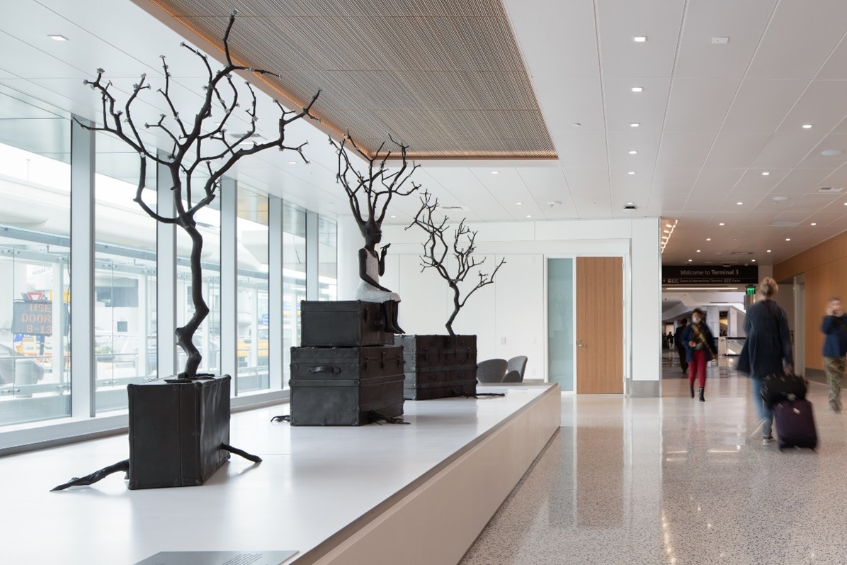 airport hallway with tree sculpture artwork with airport travelers walking