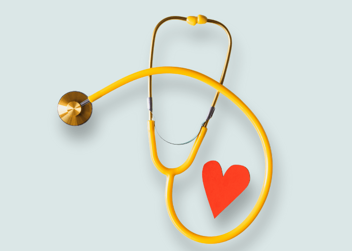 a red paper cutout of a heart framed by a yellow stethoscope on a flat surface