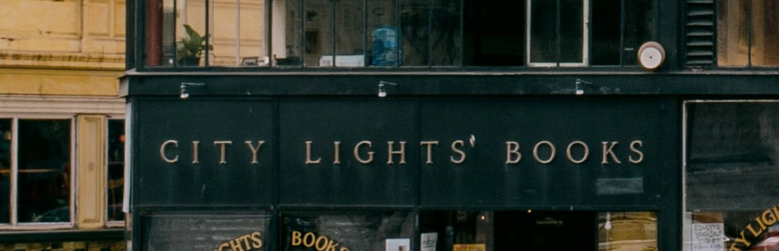 A wall sign consisting of large lettering installed on the side of a building, with 3 lamps on the building positioned on the left, middle, and right sides above the sign shining down directly on the letters.